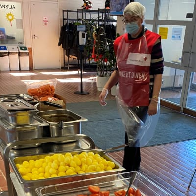 SPR:n punaiseen liiviin pukeutunut nainen aikoo jakaa ylijäämäruokaa tarvitseville koulun aulatiloissa.