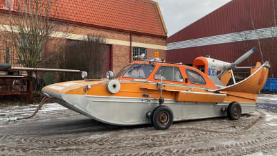 En orange hydrokopter framför gårdsbyggnader.