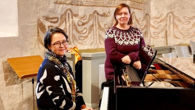 två kvinnor runt en flygel i en kyrka