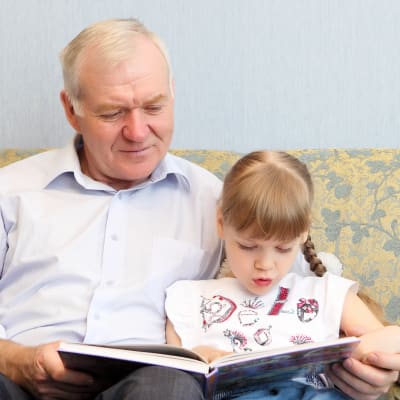 Äldre man och flicka läser en bok tillsammans i soffan. 