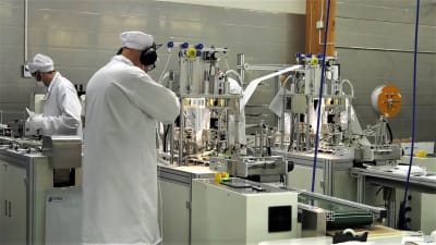 en människa i vit skyddsdräkt som jobbar på fabrik.