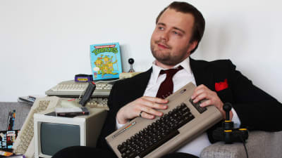 Toimittaja Antti Melkko sliipattuna, pukuun pukeutuneena, vanhan Commodore 64 konsolin kanssa.
