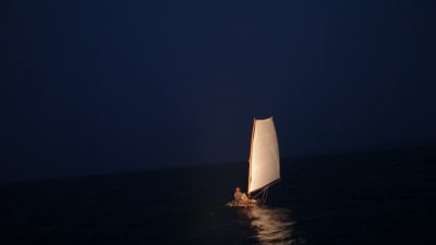 Pieni purjevene öisellä merellä, purjehtimassa yksi mies.