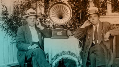 Kaksi nuorta miestä kuuntelee puutarhassa kannettavaa matkagramofonia noin 1920-luvun lopulla.
