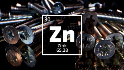 Symbolen för Zink, Zn. I bakgrunden skruvar av zink.  