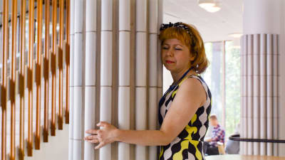 Nainen halaa Alvar Aallon suunnittelemaa, valkoisella keramiikalla pinnoitettua pylvästä.