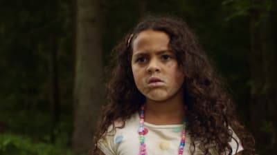 Een liten flicka med utslaget hår tittar frågan på något i skogen.