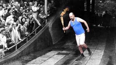 Toimittaja Olli Haapakangas juoksee olympiasoihtu kädessä yleisön edessä. 