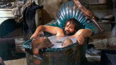 Parrakas, tukeva mies (näyttelijä Bud Spencer) makaa nukahtaneen näköisenä kylvyssä metallisessa 1800-luvun ammeessa, jonka päätyyn on ripustettu asevyö ja revolveri. Kuva elokuvasta Trinity ratsastaa jälleen.