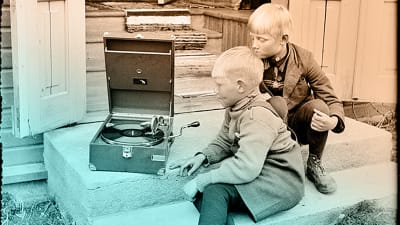 Kaksi pikkupoikaa kuuntelee gramofonia tuvan rappusilla noin 1930-luvulla.