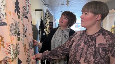 Kaksi naista tutkii museossa seinällä roikkuvaa vaatekuosia.