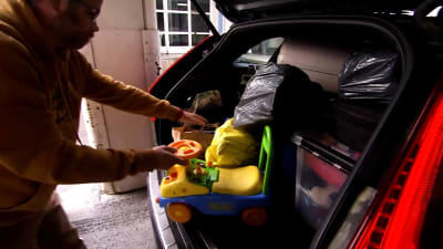 En man drar en leksaksbil ur en fullastad bilbaklucka.