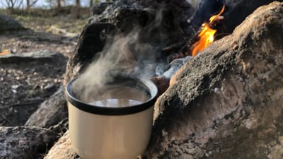 En termosmugg med kaffe vid en lägereld.