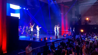 Fyra personer står och dansar på en scen och publikhavet framför dansar med.