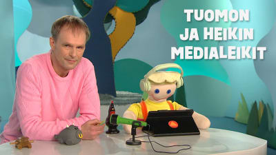 Tuomo Rannankari ja Heikki-nukke seisovat pöydän takaa. Kuvassa lukee Tuomon ja Heikin medialeikit.