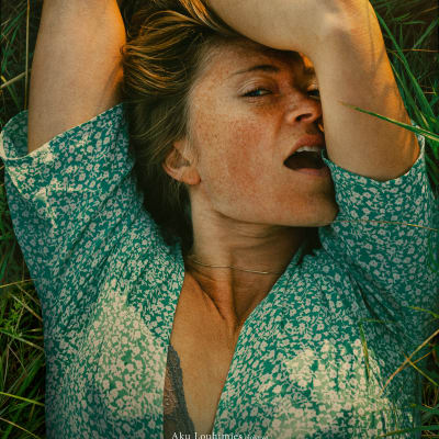 En kvinna som ligger i gräset och njutningsfullt tittar in i kameran.