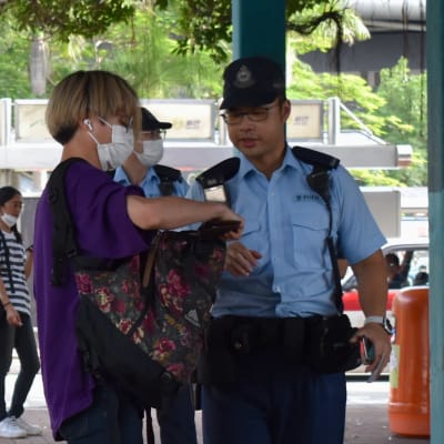 Person med munskydd visar upp innehållet i sin väska för en poliskonstapel.