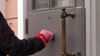 Närbild på en ytterdörr och en vante som knackar på