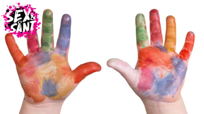 ett dagisbarns händer uppe i luften, täckta av olika färger