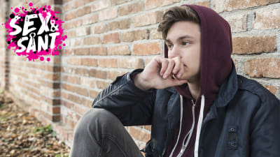 en ung man som sitter ute och lutar mot en vägg och ser bekymrad ut