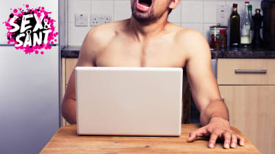 en man som sitter vid ett bor, ser på sin dator och masturberar