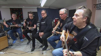 Fem mogna män sjunger och spelar gitarr