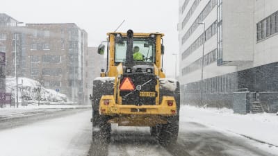 Lumiauaraustraktori ajaa tiellä lumisateessa