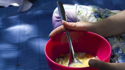 En skål med fisksoppa i ett barns händer. Barnet verkar sitta på en blå filt.