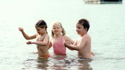Tre barn simmar på en strand