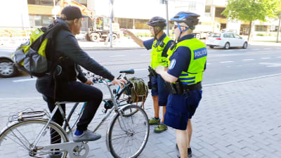Cyklist på trottoaren stoppas av två poliser. 
