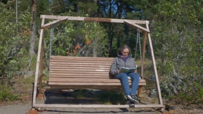 Eva Hietanen läser i en trädgårdsgunga