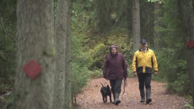 Laura Räsänen och Pekka Poutanen som går längs en naturstig med en hund. 