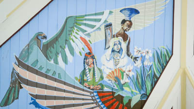 Kirkasvärisiä maalauksia kirkon katossa, papukaija, eri etnisiä ryhmiä edustavia enkeleitä.
