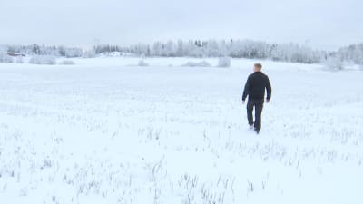 En man går på en snöig åker. 