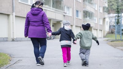 En mamma går hand i hand med två barn