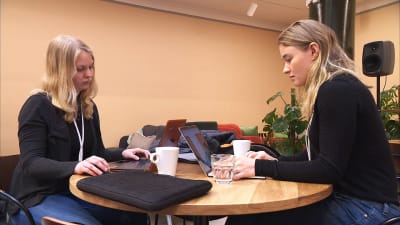 Amanda Rejström och Anna Eriksson sitter vid ett runt bord och arbetar vid bärbara datorer. 