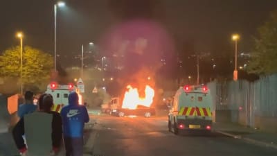 På bilden brinner en bil i londonderry. Tre åskådare syns i förgrunden.