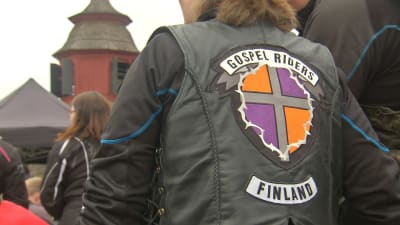 En motorcyklist med texten "Gospel Riders Finland" bak på sin läderrock står vid en kyrka.
