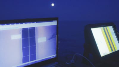 Scanners och ekolod i öppen båt på natten i månsken ute på havet.