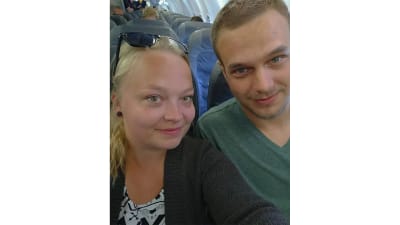 Paret Hanni och Joni sitter i ett flygplan och tar en bild på sig själv med blickarna riktade rakt mot kameran.