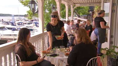 En servitris serverar mat åt två kvinnor som sitter vid ett bord på en uteservering.