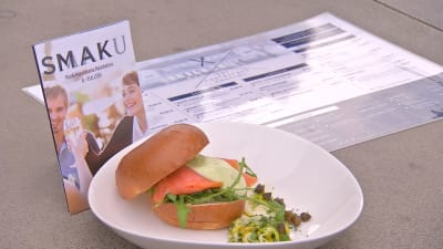 En broschyr för Smaku-matfestivalen och en hamburgare på en tallrik.