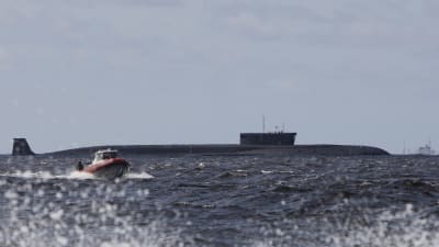 En ubåt ligger i vattnet. I förgrunden syns en motorbåt. Det är sjögång.