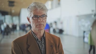 Jan Löfstedt intervjuas i biblioteket Oodi. Han har en brun kavaj och rutig skjorta på sig.