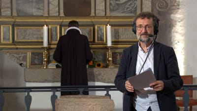 TV-regissören Flemming Stentoft står med hörlurar på huvudet framför altare i dansk kyrka.