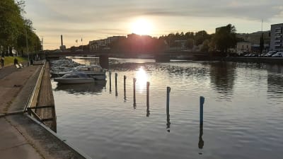 Solen går ner och speglas i Aura ås vatten i Åbo, där båtar ligger förtöjda i ån.