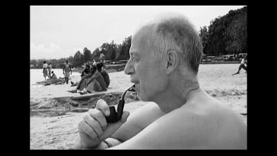 Thomas Elfgren sitter på en strand i Rwanda och röker pipa.