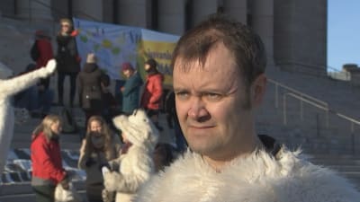 Jaakko Aarniala, aktivist, framför riksdagshuset i Helsingfors tillsammans med andra miljöaktivister som syns i bakgrunden.
