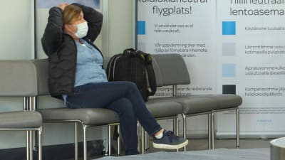 En kvinna med ansikstmask sitter och väntar på sitt bagage på flygplatsen