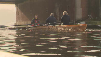 En roddbåt med tre personer i åker under en bro i Amsterdam. 